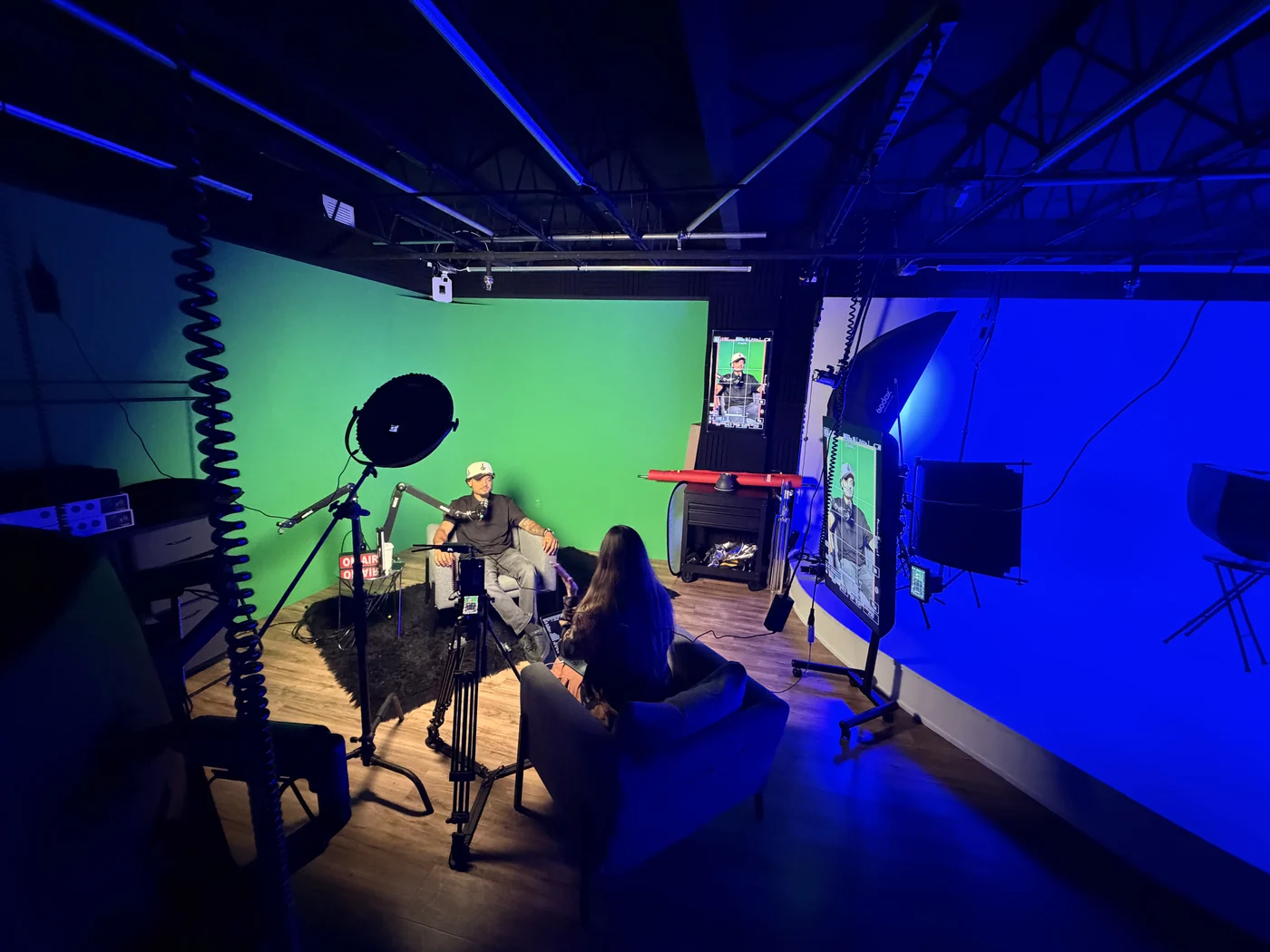 El set de podcast desde el fondo de la sala, con luz azul y verde